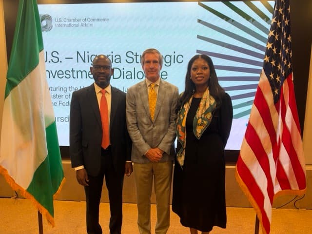 Three speakers on stage in front of the dialogue backdrop, flanked by the Nigerian and American flags